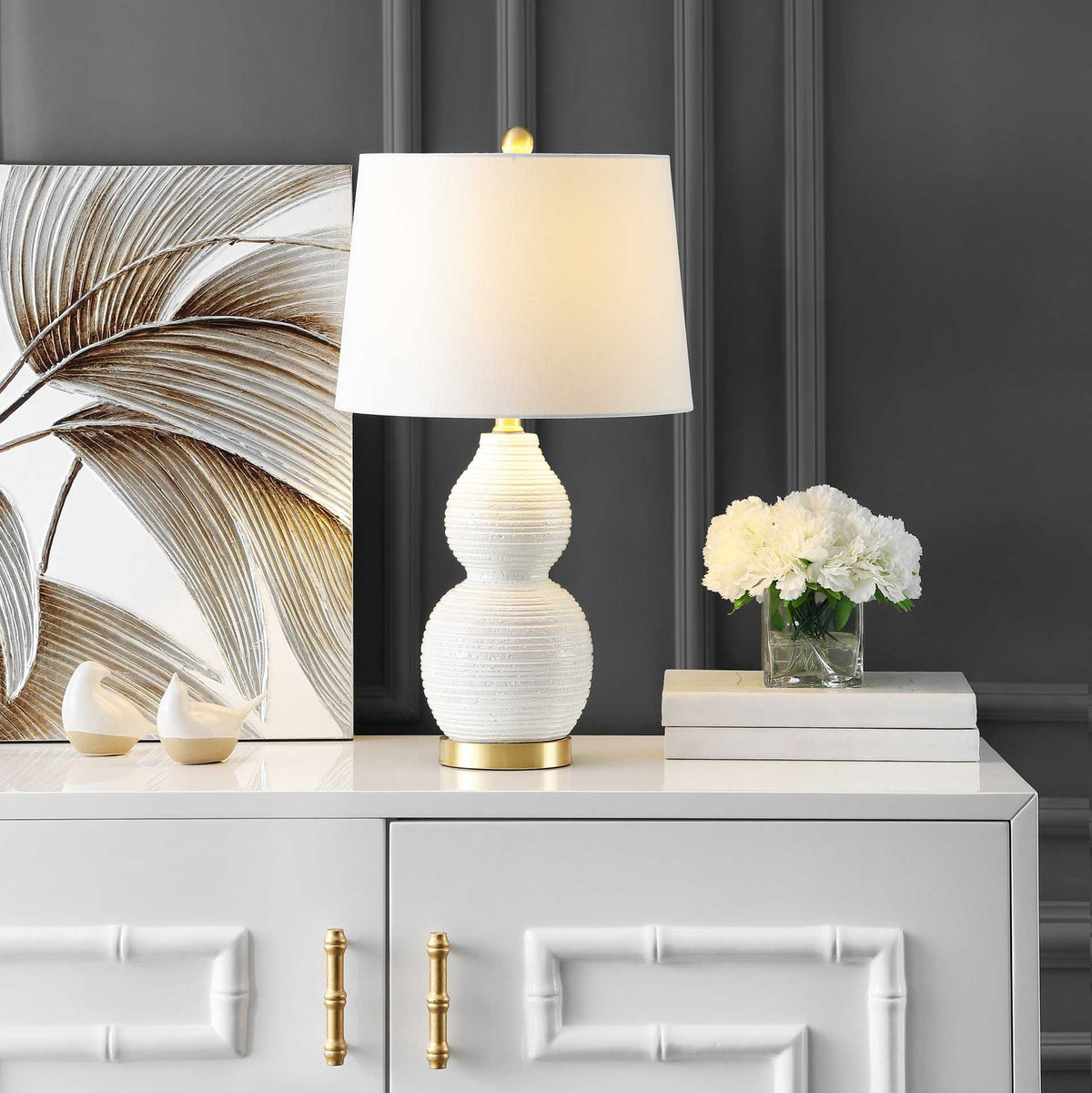 A soft glow highlights the white shade, ribbed ceramic base, and gold-tone details