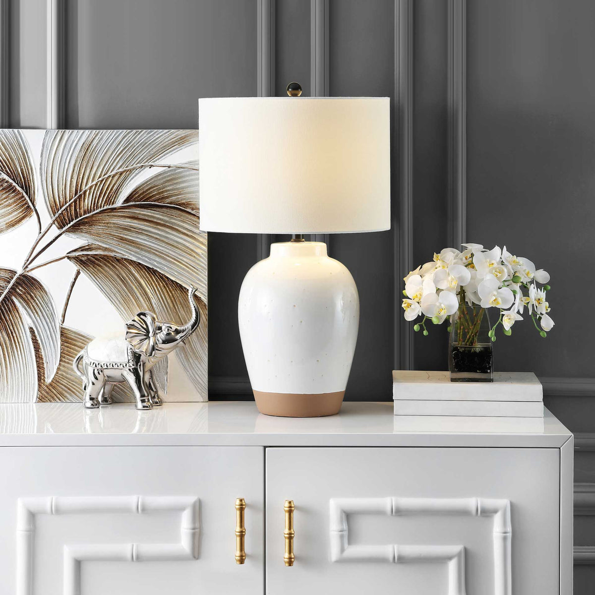 A softly glowing white drum shade tops the speckled ivory ceramic lamp on a white cabinet