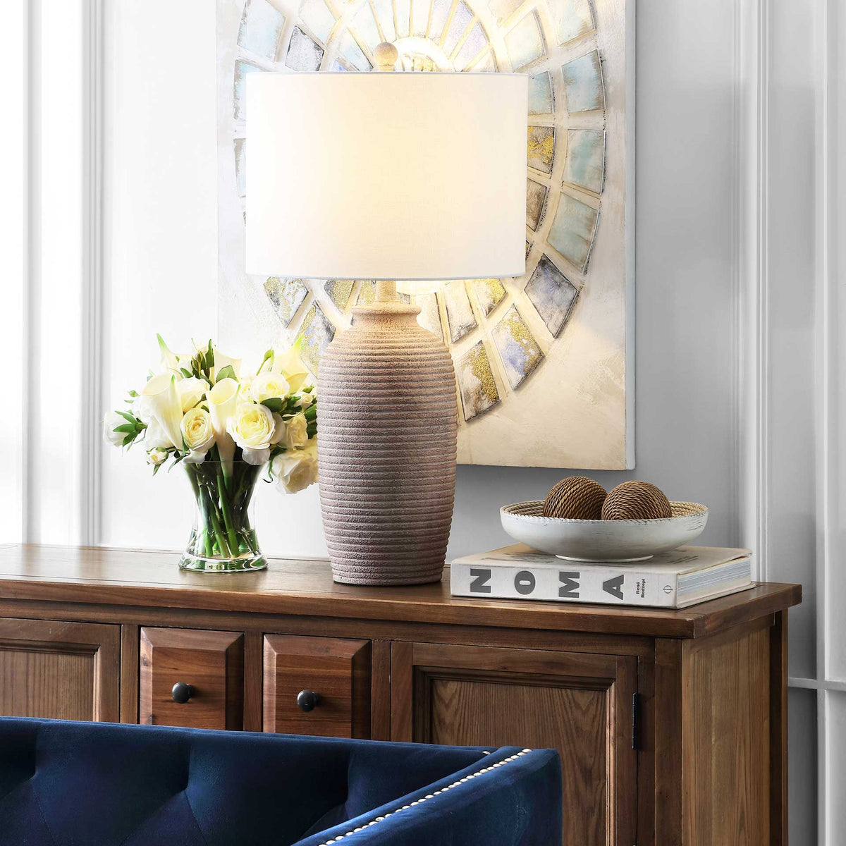 Warm light from the white drum shade highlights the lamp's sandy pearl, ribbed resin base