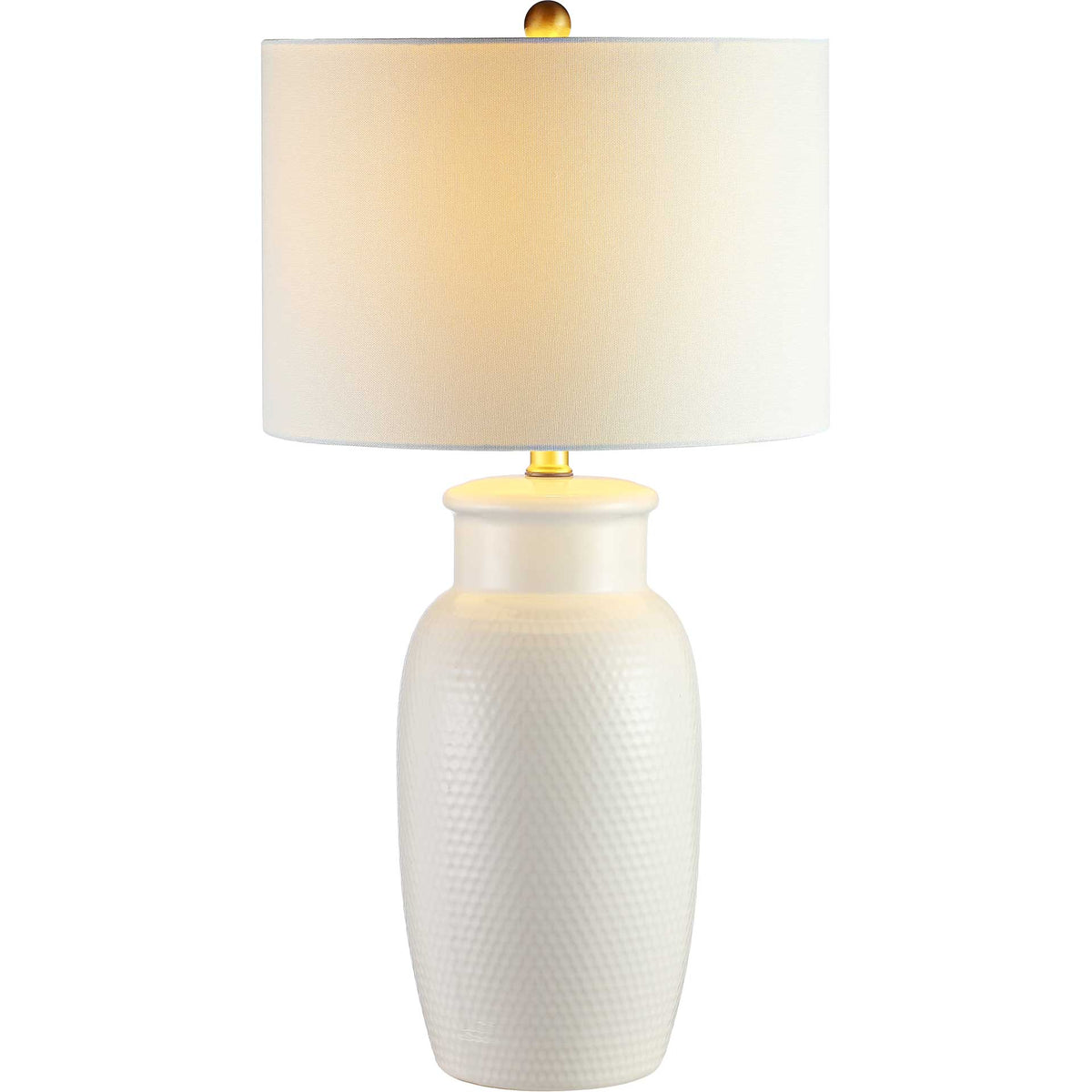 Warm light glows through the white drum shade above a patterned ivory ceramic base.