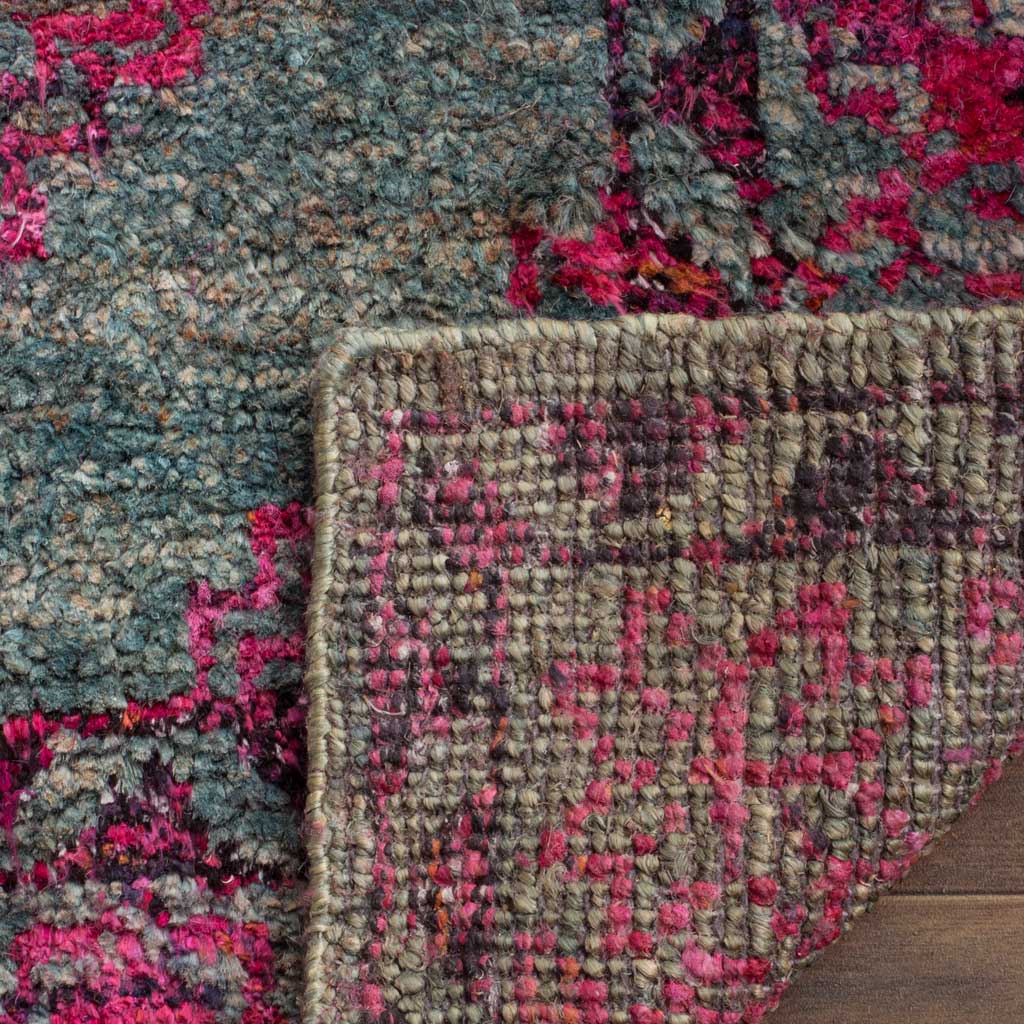 Folded rug corner reveals its woven backing beneath textured slate blue and fuchsia fibers