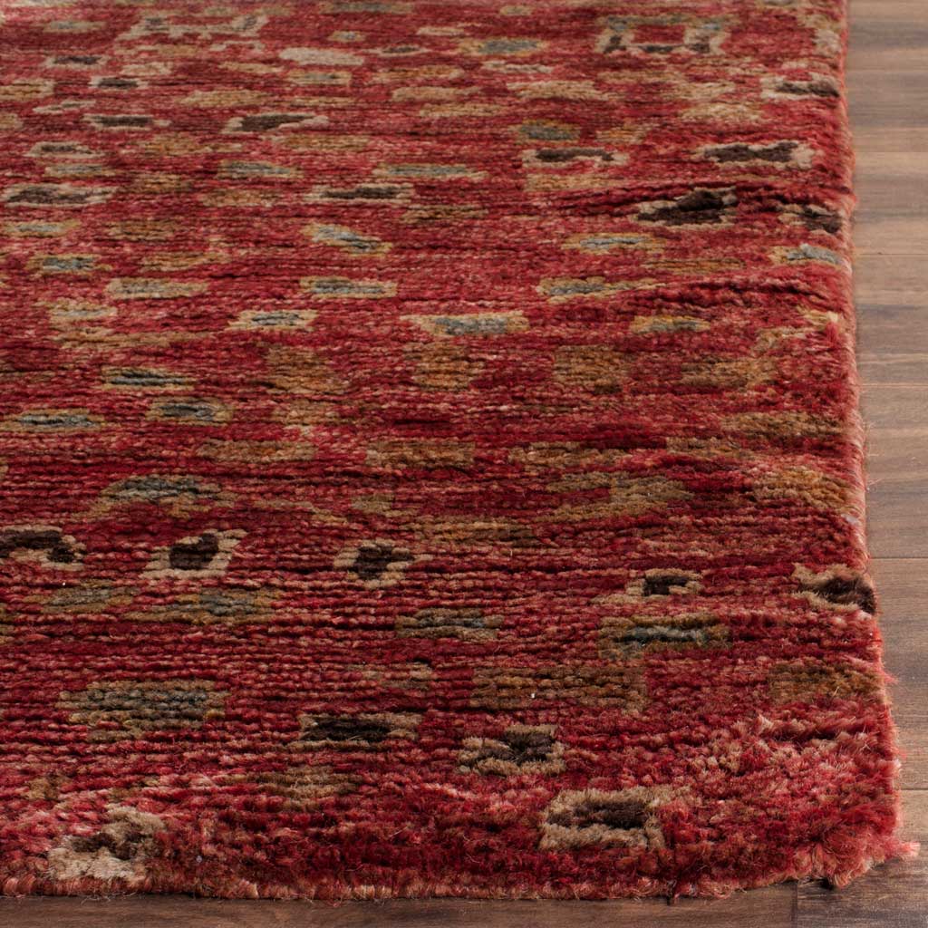 Dense red pile blends rust, gold, and charcoal accents along the rug's finished corner