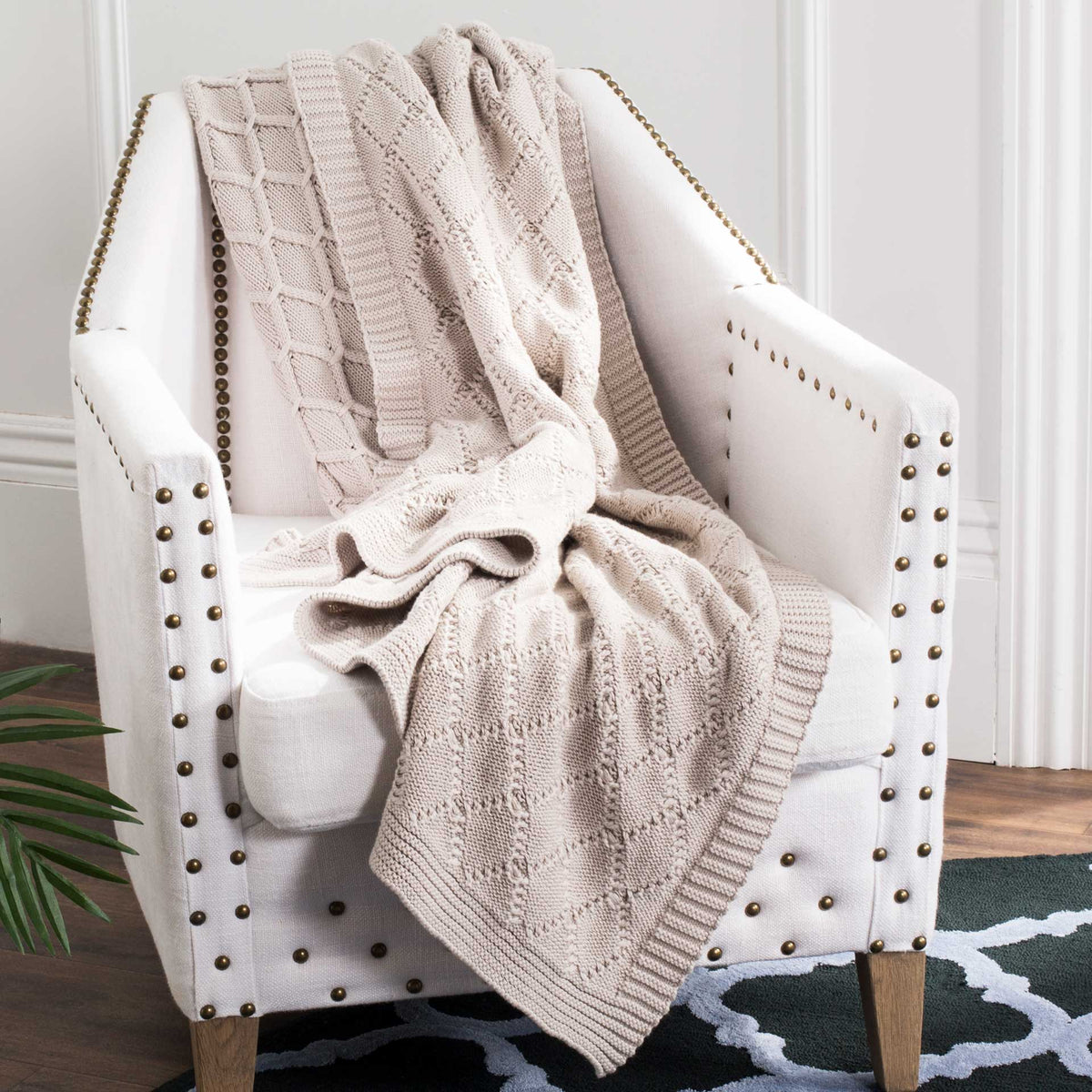 Pale pink knit throw drapes in soft folds, showing its cable pattern and ribbed border
