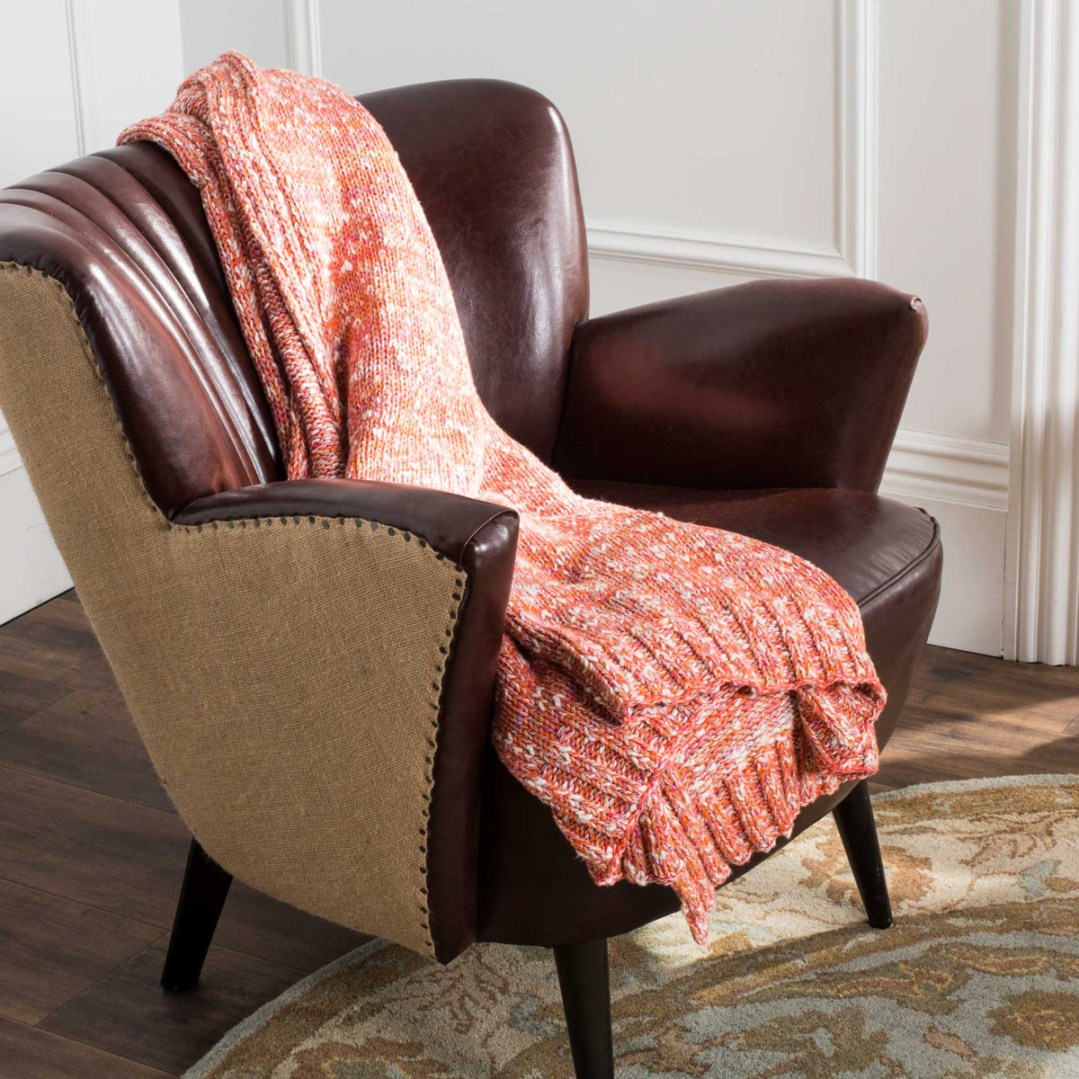 A coral-toned knit throw drapes across a leather chair, adding cozy color and textured folds.
