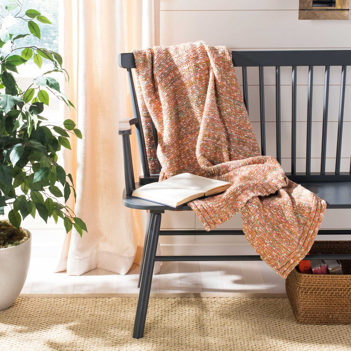 Warm coral and cream yarns give this knit throw inviting texture against a dark wooden bench.