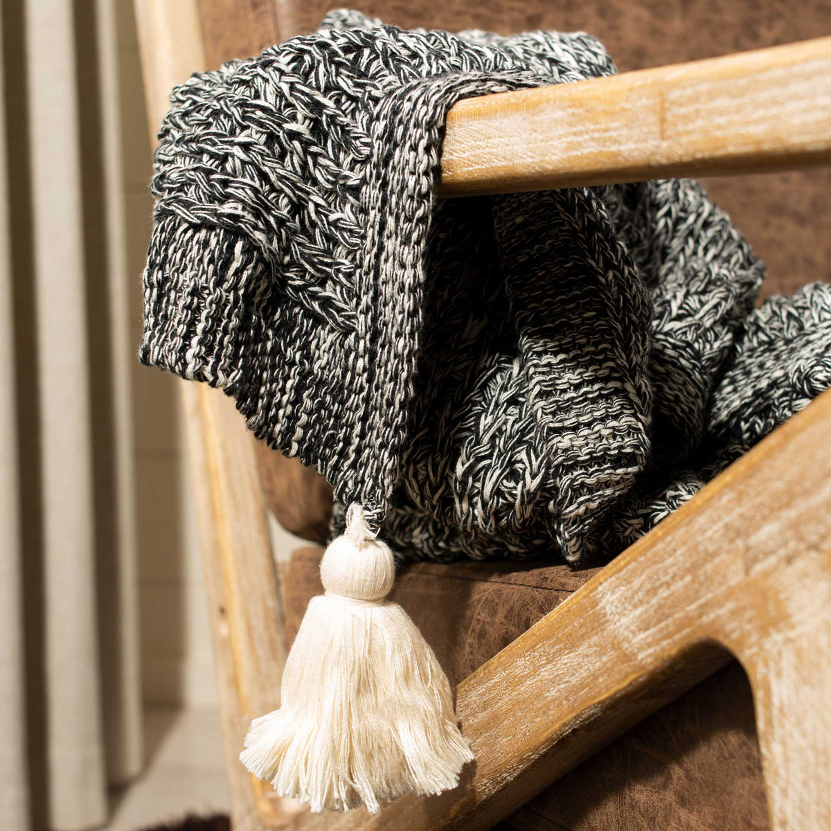 Textured black and natural knit features a thick border and a full cream tassel.