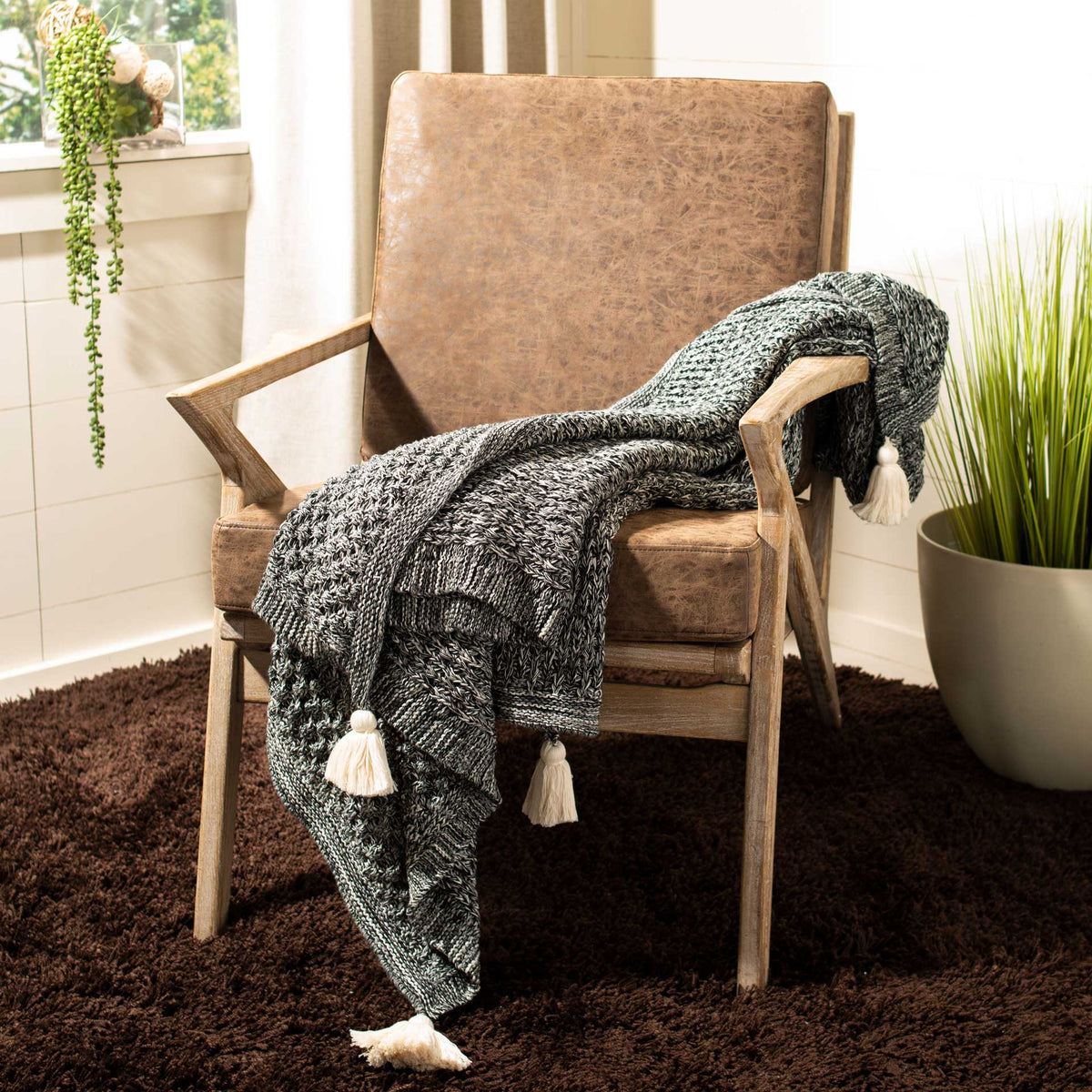 Black and natural knit throw drapes over a chair, with cream tassels adding a playful finish.