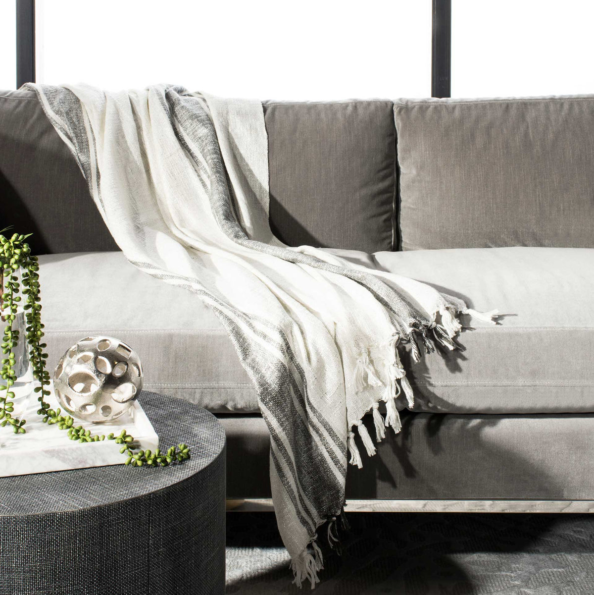 A white and gray tasseled throw brings cozy woven texture to a modern sofa