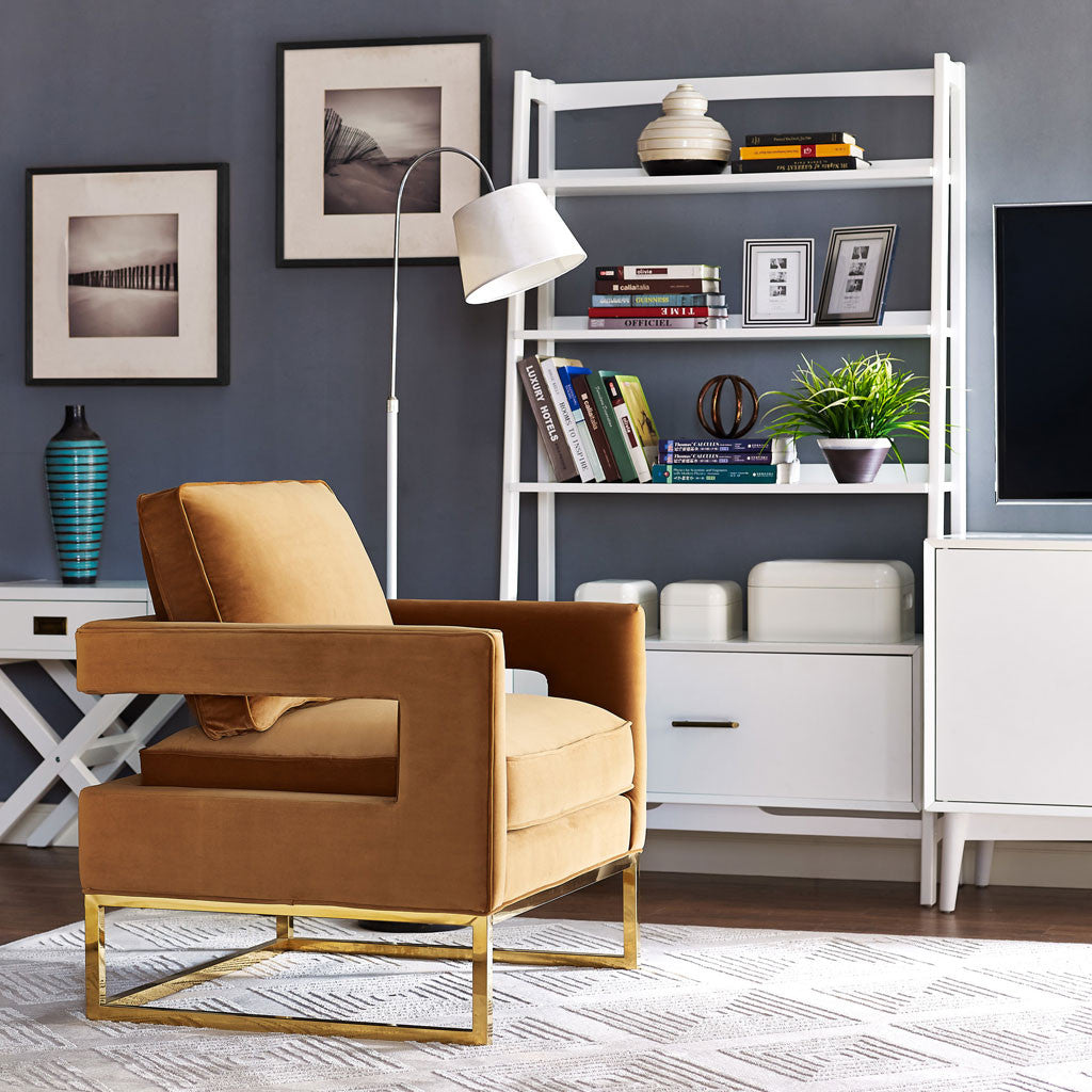 Rich cognac velvet, airy arm cutouts, and slim gold sled legs bring cozy sophistication to a reading nook.