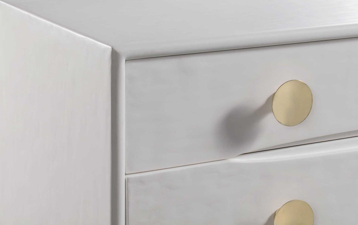 Round brass knobs stand out against softly rippled white drawer fronts
