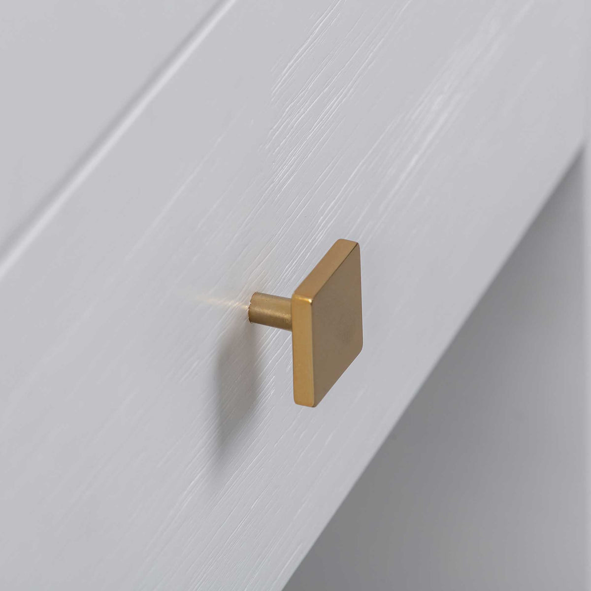 A square gold-tone knob adds a warm metallic accent to the white wood-grain drawer front.
