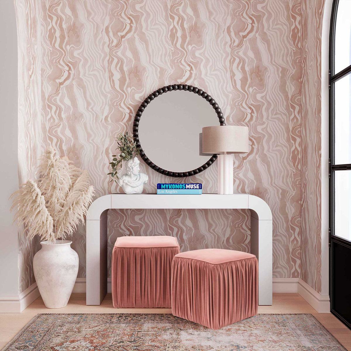 A black beaded mirror adds striking contrast above a curved white console in a pink room.