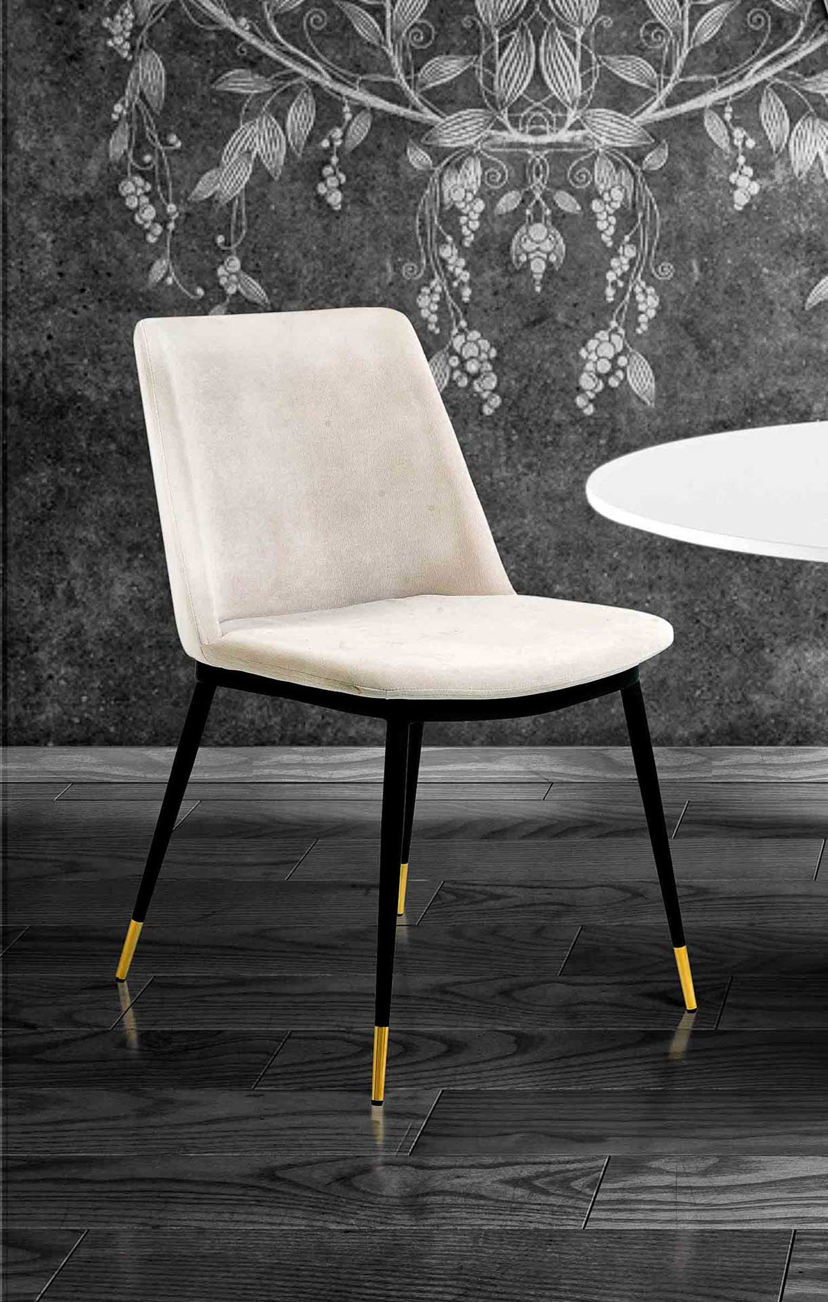 A cream velvet dining chair brings soft contrast to dark decor with black legs and gleaming gold tips.