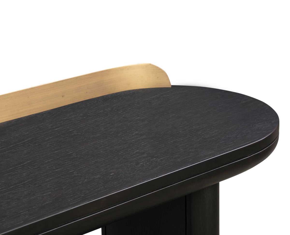 Textured black wood grain meets a smooth rounded edge and a softly curved brass-finished rail