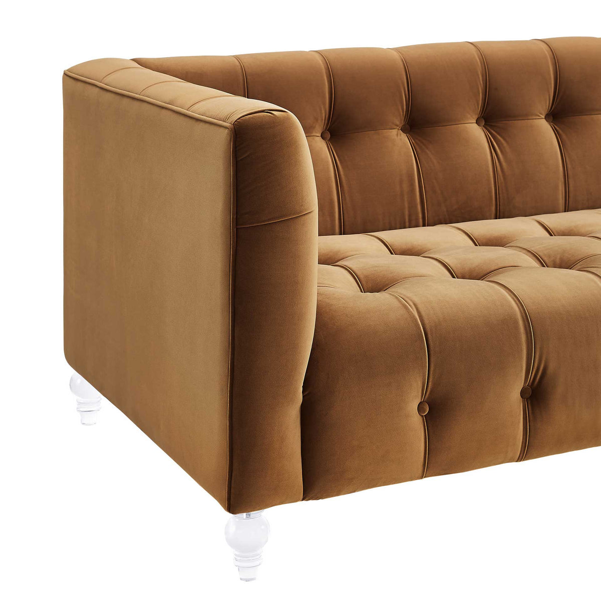Rich cognac velvet wraps a padded arm, with deep seat tufting and a sculpted transparent leg