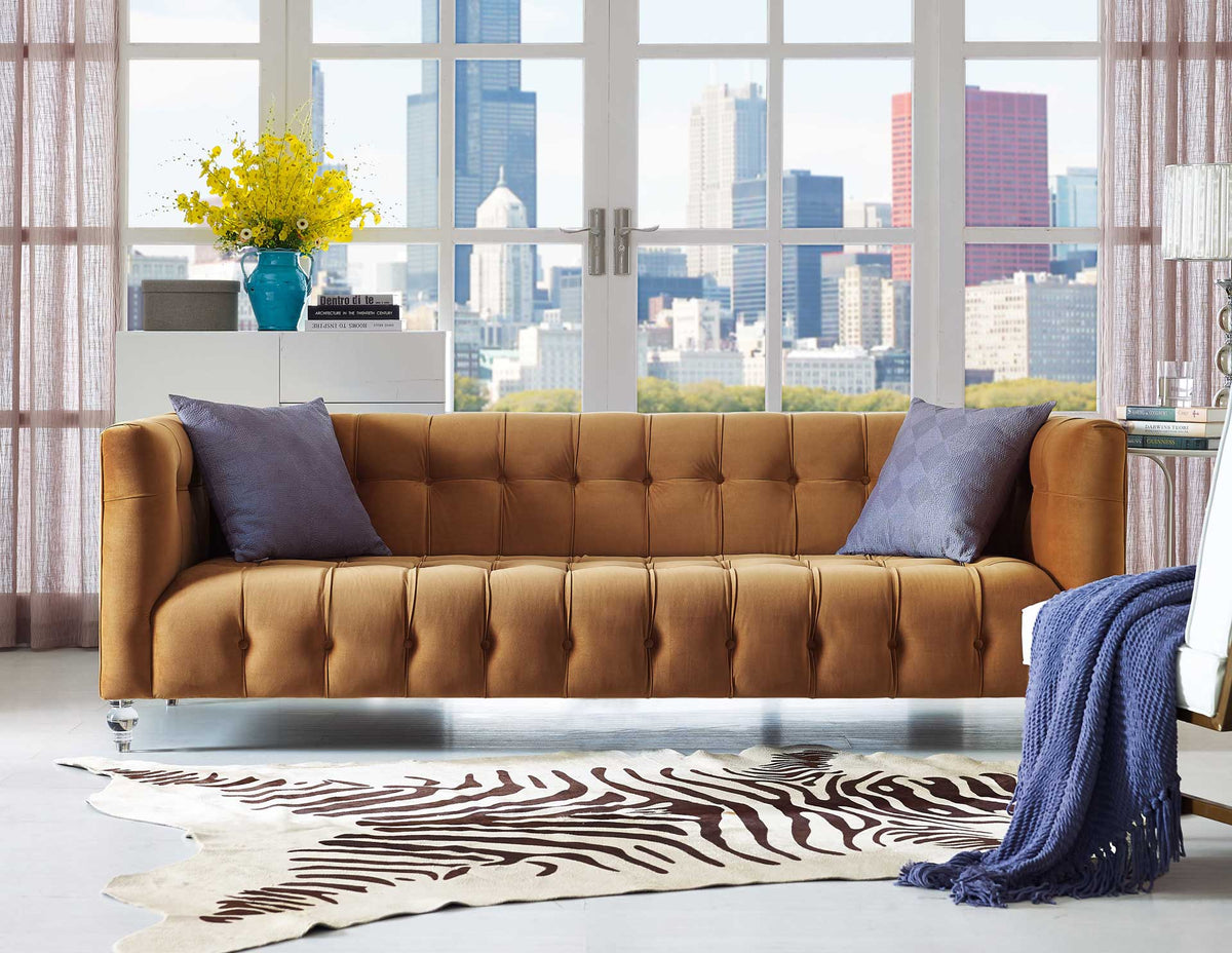 Warm cognac velvet and plush tufting bring inviting comfort, complemented by contrasting accent pillows