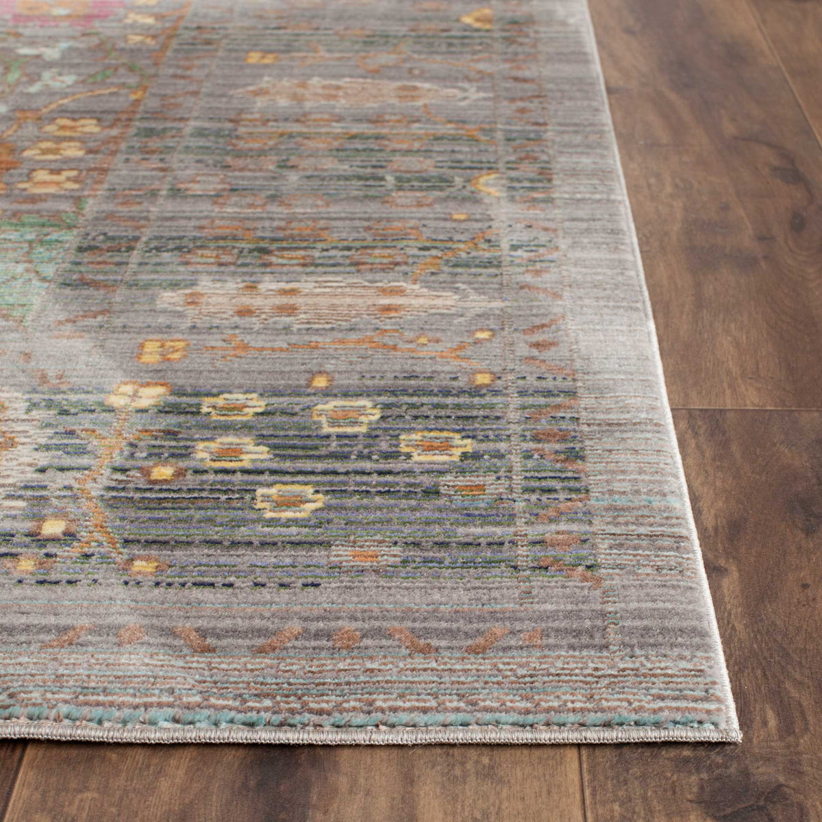 A neatly finished rug corner highlights the low gray pile and subtle orange, teal and gold threads.