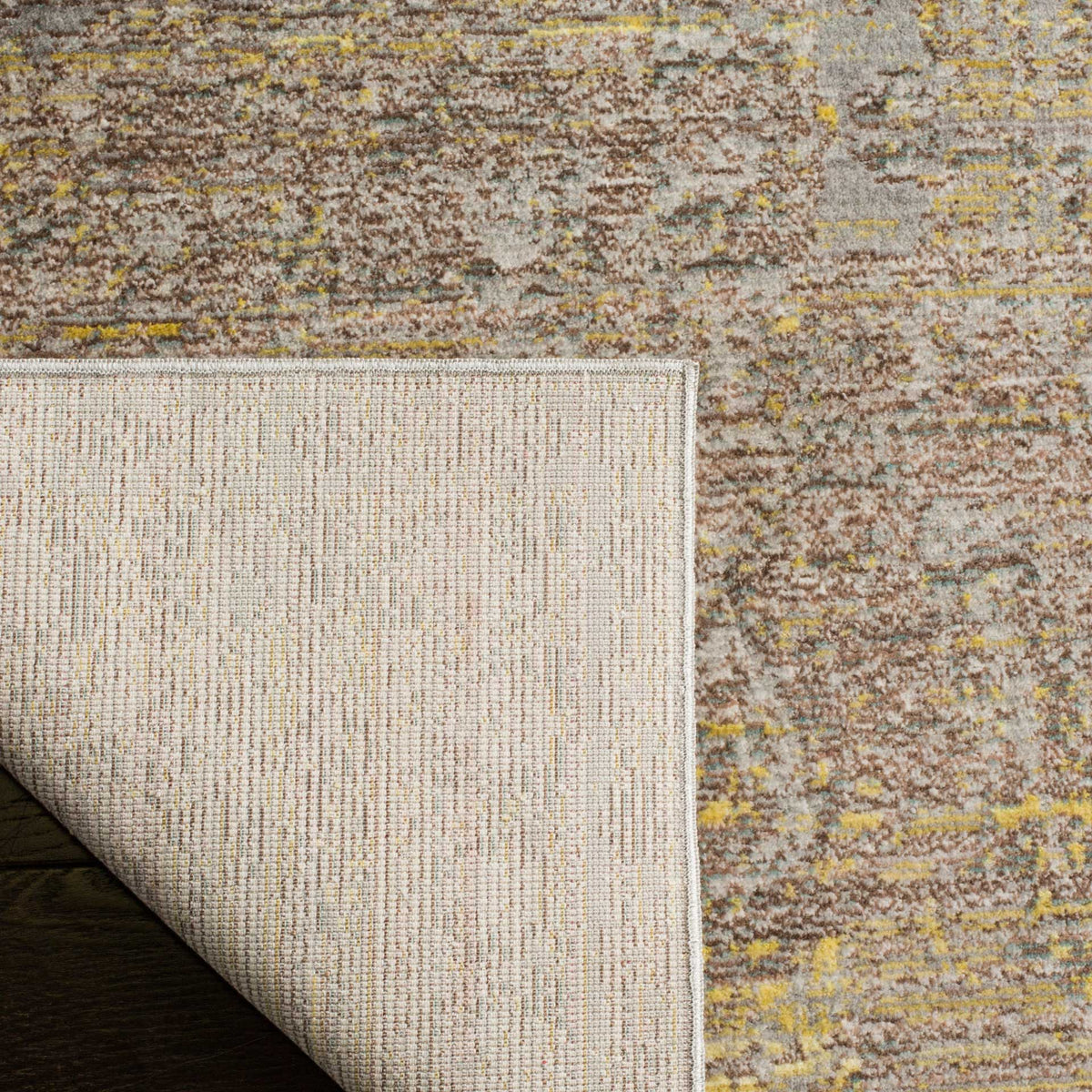 A folded corner reveals woven cotton backing beneath the muted gray and gold pattern.
