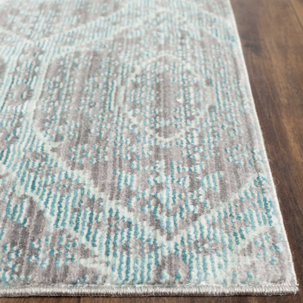 Neatly bound edges finish the rug's low, textured pile and intricate aqua pattern.