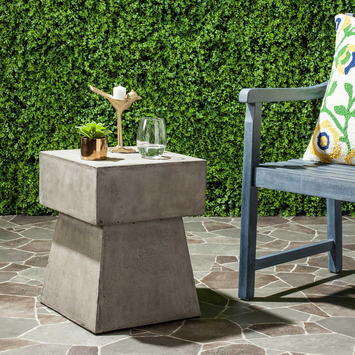 Dark gray concrete side table holds drinks and decor beside outdoor seating