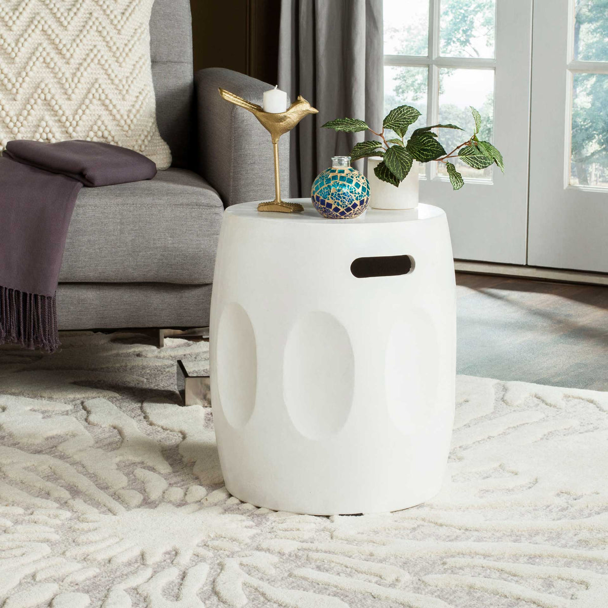 Ivory accent table offers a round surface, recessed handhold, and oval detailing beside a sofa