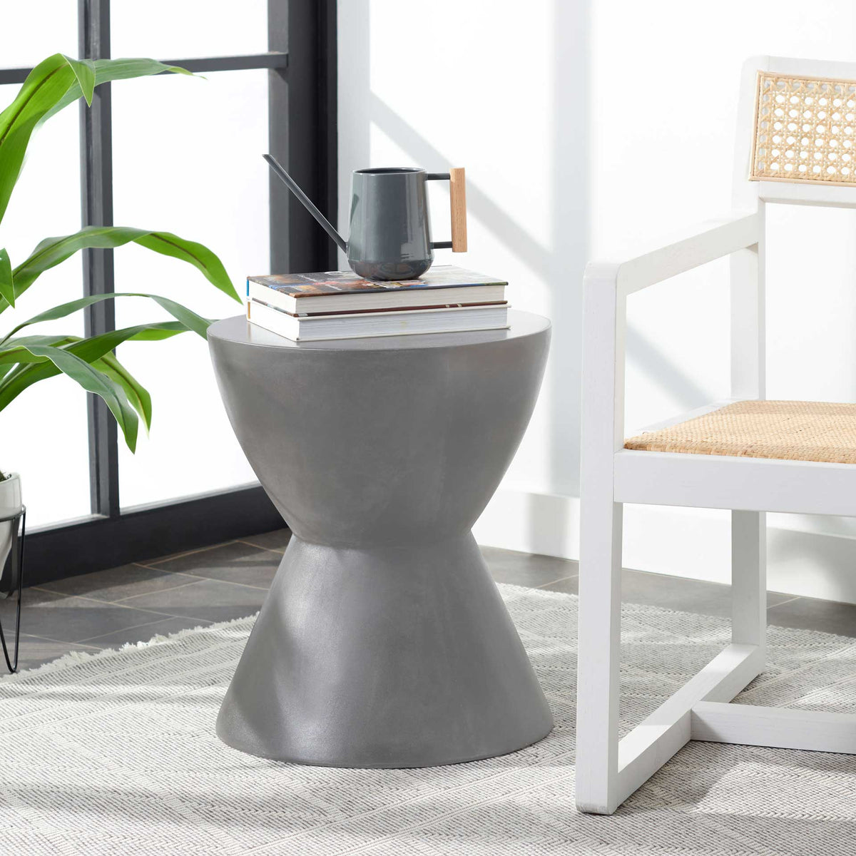 Sculptural dark gray accent table holds books and a watering can beside a modern chair