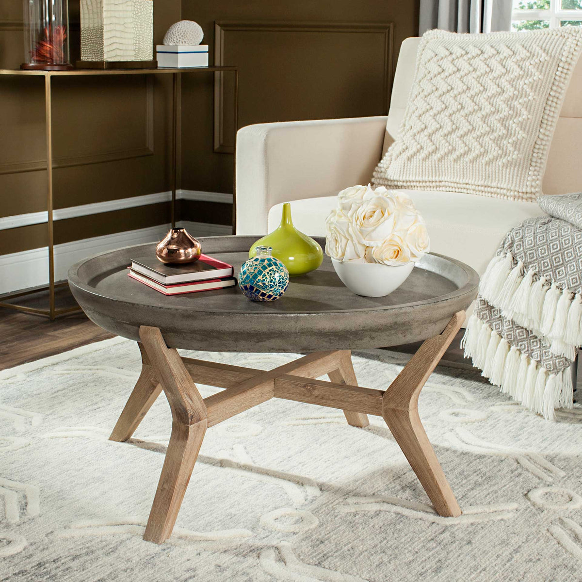 A round concrete coffee table with a raised rim and sculptural wood base anchors a living room