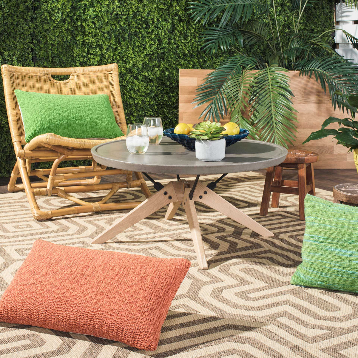 A round concrete coffee table on splayed oak legs anchors a relaxed outdoor seating area.