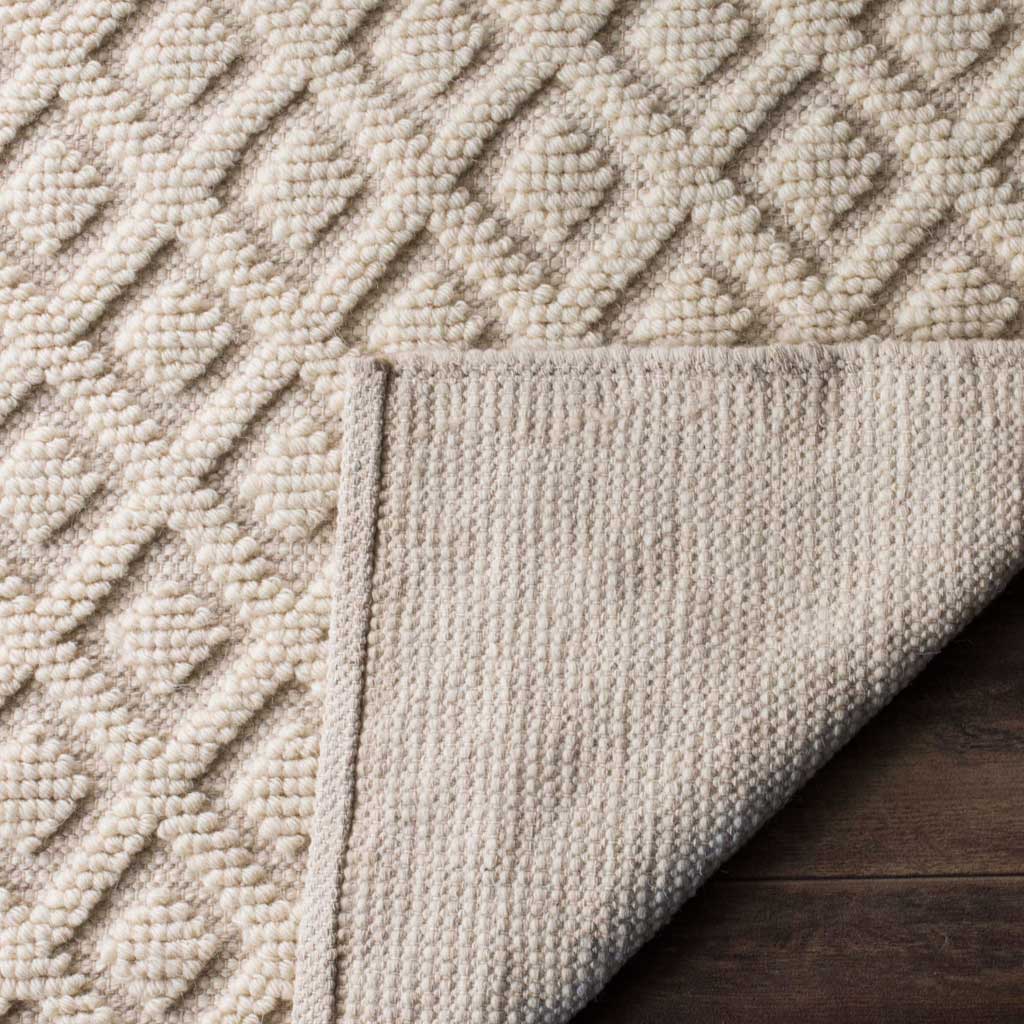 A folded corner reveals the rug's woven underside beneath its raised diamond texture.